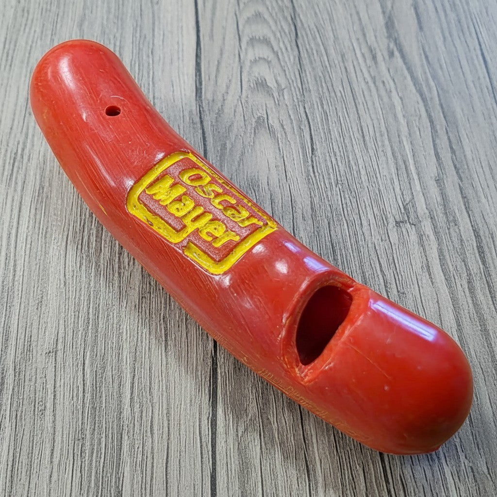 Jones Peak red plastic hot dog novelty whistle with yellow Oscar Mayer logo, 2 inches long.