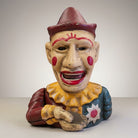Jones Peak clown cast iron mechanical coin bank with hand-painted antique patina, red hat, yellow ruff, and teal costume.